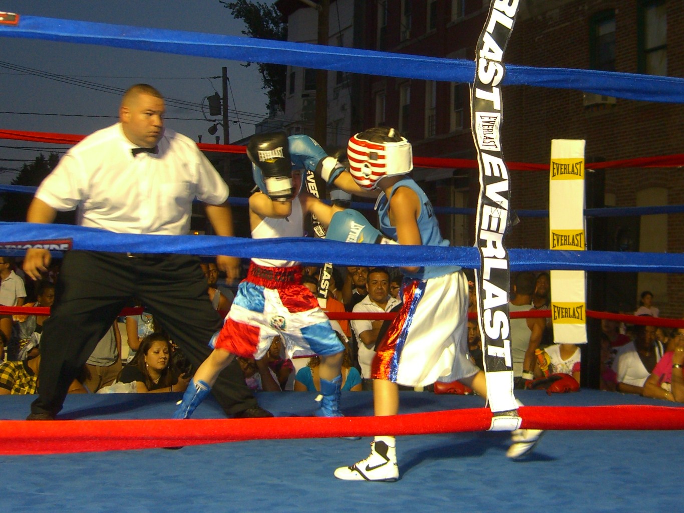 A referee and two young boxers sparring in a ring while spectators watch