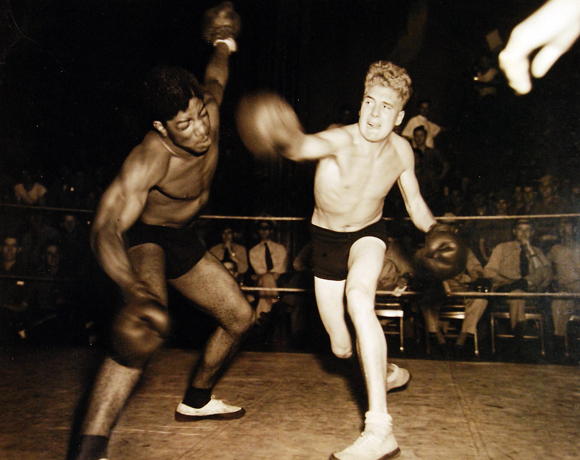 Two boxers fighting inside a ring in front of a live audience