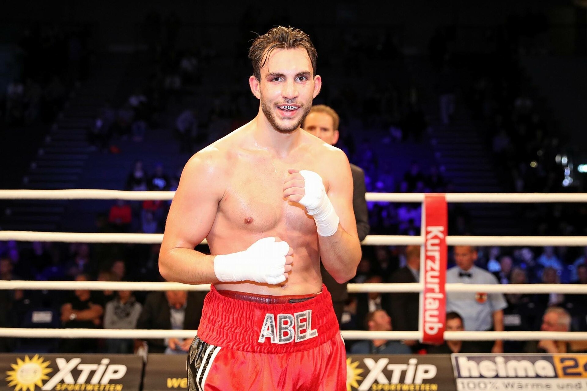 A boxer standing in the ring wearing red trunks with his hands wrapped
