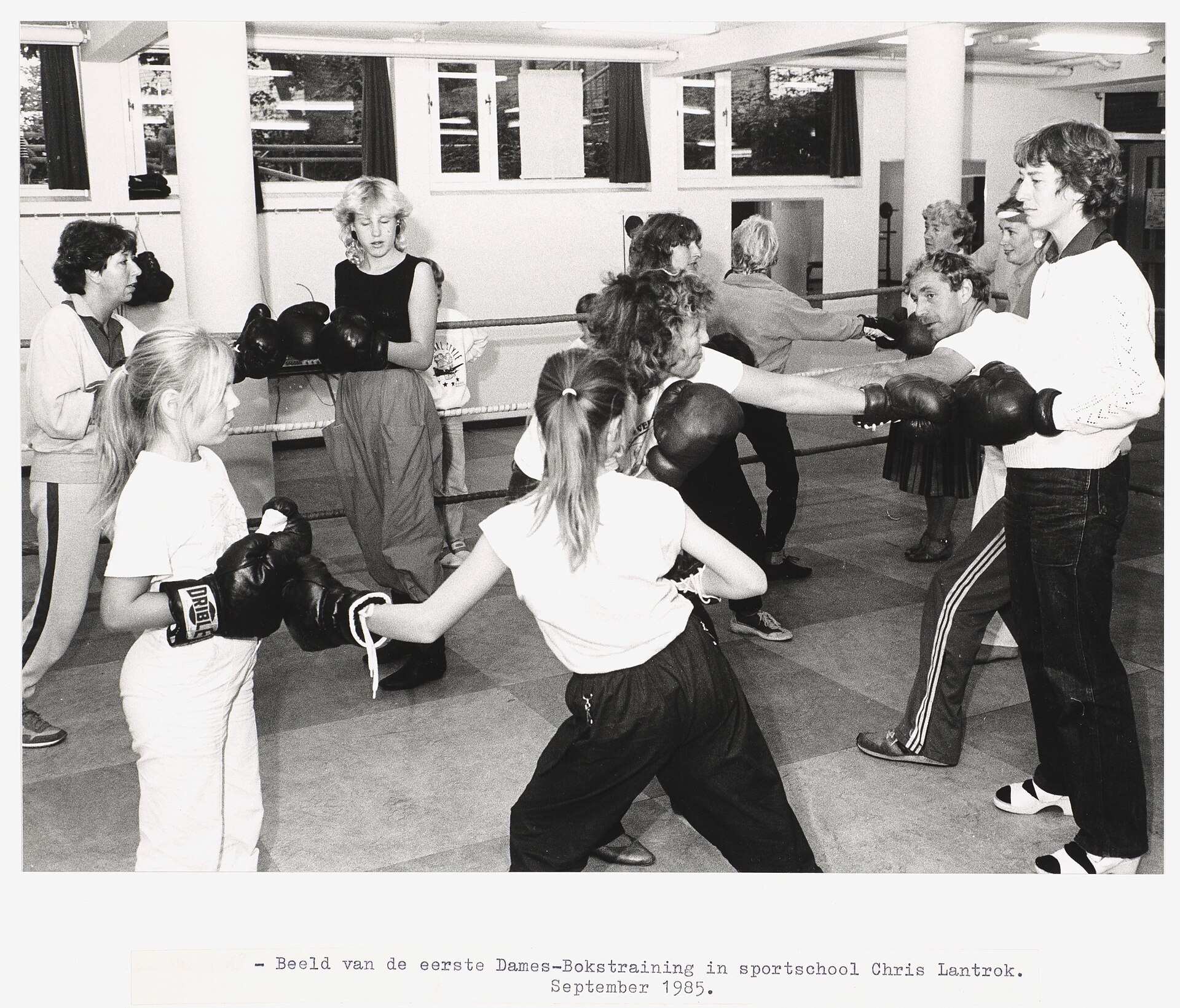 A black and white photograph of a group of women and children practising boxing moves in a gym